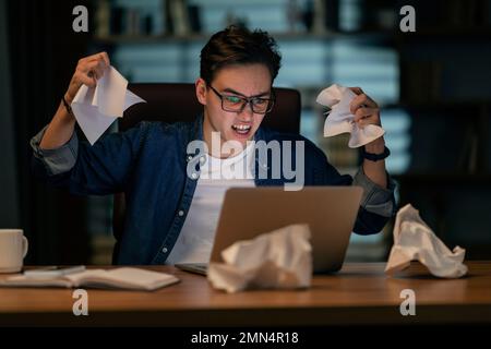 Furious emotional young man working at office late at night Stock Photo