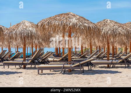 Straw beach umbrellas and sun loungers by the sea. Stock Photo