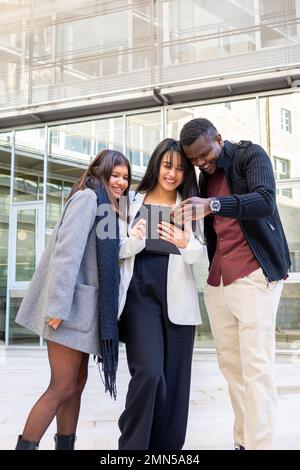 Attractive coworkers using a tablet outside the office. Group of young friends smiling at work outdoor in the city. Ethnic diversity, social inclusion Stock Photo