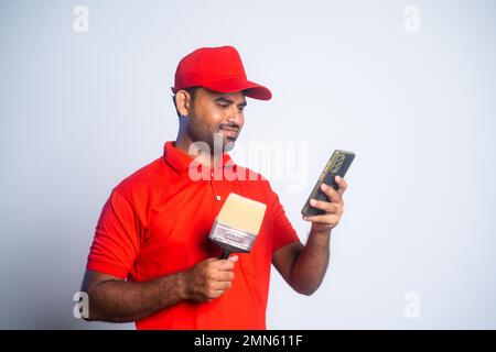 Happy painter busy using mobile phone by holding paint brush at construction site - concept of social media, technology and relaxation Stock Photo