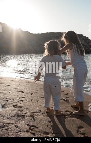 Two girls are smiling and playing on vacation at the sea near the rocks. Children play and rejoice. Friendly family at home and on vacation. Stock Photo