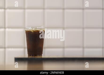 Closeup of takeaway plastic cup of iced black coffee Americano on wooden table in restaurant. Stock Photo