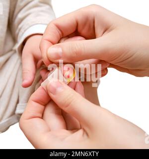 Woman mother sticks a medical band-aid on the toddler baby finger, isolated on a white background. Mom s hand with a sticky wound protection bandage a Stock Photo