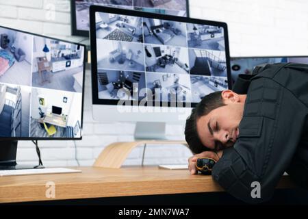 Male security guard sleeping near monitors at workplace Stock Photo