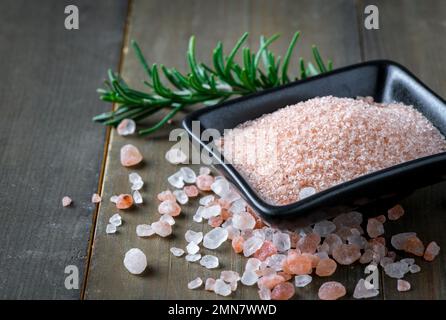 Himalayan Rock pink Salt in black bowl and rosemary leaf  on wood background, Stock Photo