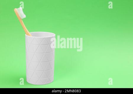 Bamboo toothbrush in holder on green background, space for text Stock Photo