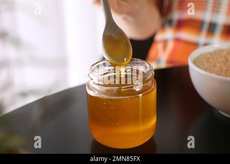 Spoon with honey over jar on black table, closeup Stock Photo