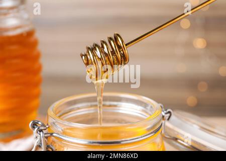 Dripping tasty honey from dipper into jar on blurred background, closeup Stock Photo