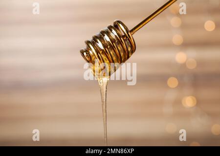 Dripping tasty honey from dipper on blurred background, closeup Stock Photo