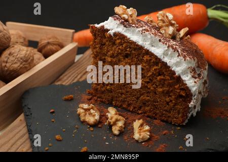 Portion of a carrot cake decorated with meringue, chocolate and walnuts, next to it we see raw carrots and walnuts with a dark background and copy spa Stock Photo