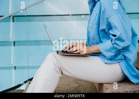 Young woman working with laptop while sitting on stairs outdoors Stock Photo