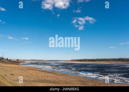 The spring river in the north of Yakutia Vilyui thaws from the ice against the backdrop of the village. Stock Photo