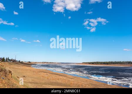 The spring river in the north of Yakutia Vilyui thaws from the ice against the backdrop of the village of Suntar and the forest. Stock Photo