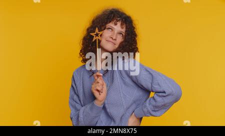 Magician witch woman gesturing with magic wand fairy stick, making wish come true, casting magician spell, advertising holidays sale discount. Young teen girl isolated on yellow studio background Stock Photo