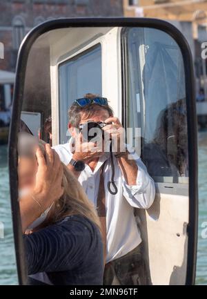 Male photographer with a camera taking a photo while reflecting in the mirror of a ship. Stock Photo