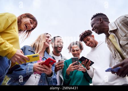 Multiracial Erasmus students, standing outdoors using their phones and laughing together. Stock Photo