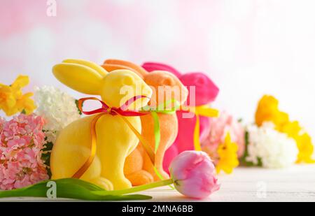 Easter decoration with Easter colorful rabbits and spring flowers on white wooden table. Easter concept with copy space. Stock Photo