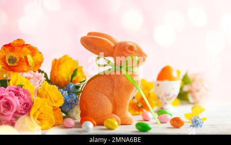 Easter decoration with Easter eggs, colorful rabbits and spring flowers on white wooden table. Easter concept with copy space. Stock Photo