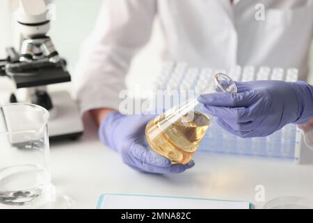 Scientist measuring yellow liquid in flask at chemical laboratory. Stock Photo