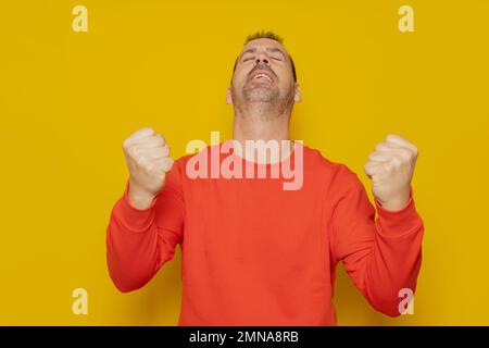Portrait of a satisfied man celebrating success with raised fists and looking up isolated over yellow background Stock Photo