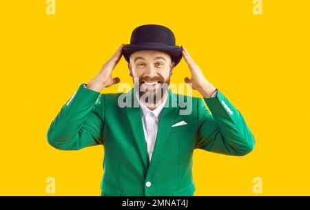 Portrait of cheerful smiling man in green jacket and black hat on orange background. Stock Photo