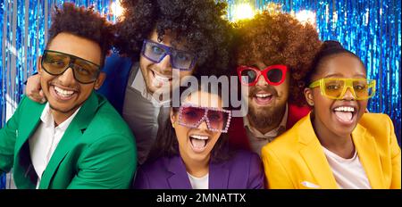 Happy cheerful multiracial people in colorful suits, disco glasses and funny wigs in photo booth Stock Photo