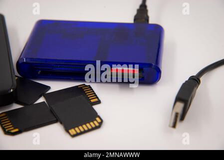 Black memory cards and external hard drive with blue card reader and card in it on white background. Stock Photo