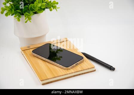 Mobile smart phone with blank screen of gadget on notebook. Digital cell phone with copy space area on white background with pencil and leaf Stock Photo