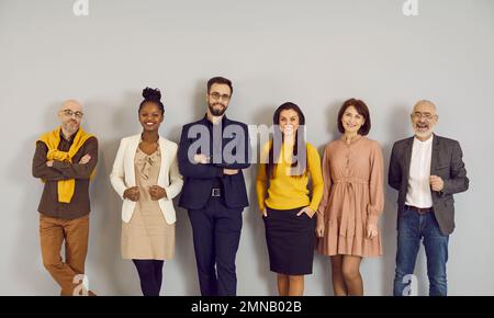 Portrait of multiracial representatives of modern business team standing in row near wall. Stock Photo