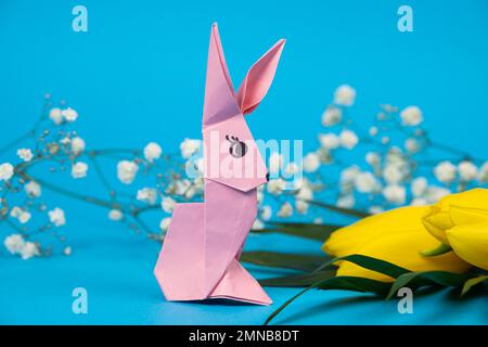 A pink and yellow origami rabbits on a blue background. Crafts for ...