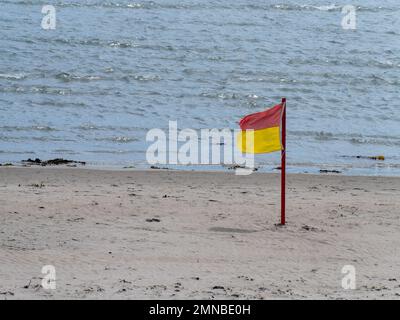 Red and yellow flag allowing swimming on the sandy seashore. Public beach. Red and yellow flag on beach shore Stock Photo