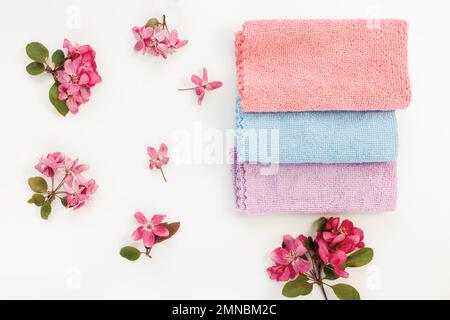 New folded microfiber cloth for cleaning on white with spring flowers background. Cleaning micro fabric towels for dusting and polishing. Domestic household cleaning service concept. Top view Stock Photo