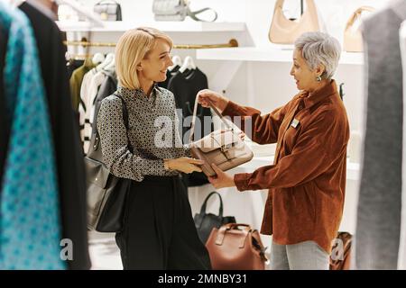 Adult mother and daughter enjoying shopping together and choosing bags at luxury boutique Stock Photo