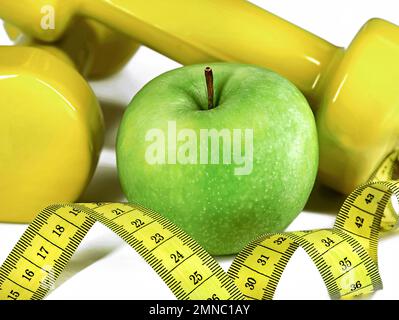 close up of measuring tape, green apple and yellow dumbbells on white background, Healthy lifestyle and fitness concept Stock Photo