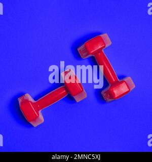 Two bright red dumbbells are isolated on blue background. Sport and health concept. Stock Photo