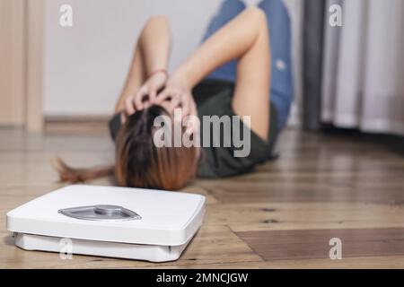 Scales and depressed young woman lying on the floor Stock Photo