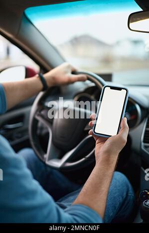 Close up Hands of unrecognizable man driver using white screen mockup mobile phone while driving Stock Photo