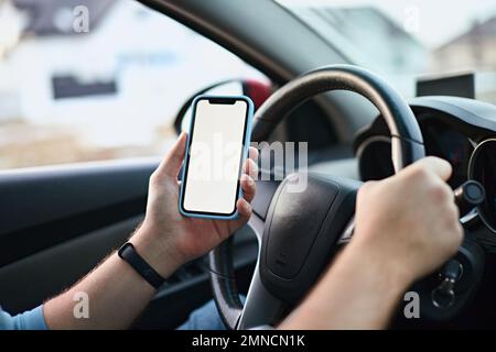 Close up Hands of unrecognizable man driver using white screen mockup mobile phone while driving Stock Photo