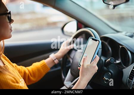 Woman driver using mobile phone screen blank mockup while driving distracted from the road Stock Photo