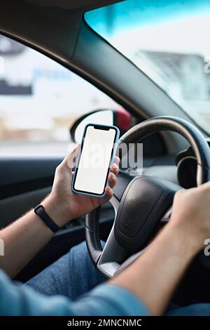 Close up Hands of unrecognizable man driver using white screen mockup mobile phone while driving Stock Photo