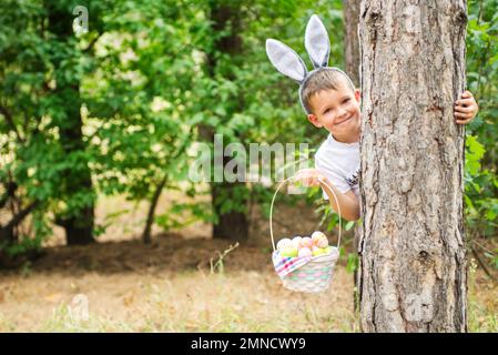 Happy child looks out of a tree holding basket full of colorful easter eggs Stock Photo