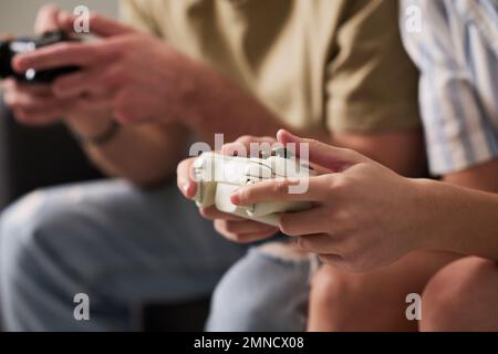 Close-up of hands of young man and woman pressing buttons on gamepads while playing video game together at leisure Stock Photo