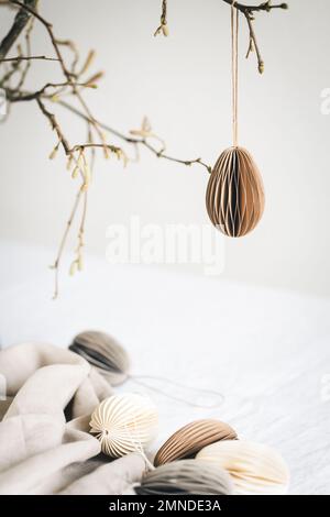 Easter paper egg hanging on branch under table with decorations. Stock Photo