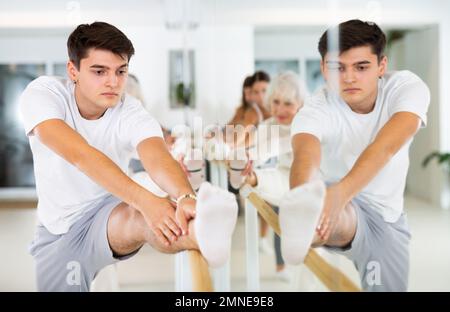 Dancer man exercise stretching on a ballet barre at a group training session in the dance studio. Stock Photo