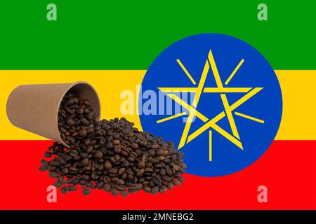 An overturned disposable paper cup filled with roasted coffee beans against the background of the Ethiopian flag (close-up) Stock Photo