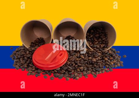 Three overturned disposable paper cups filled with roasted coffee beans against the background of the Colombian flag (close-up) Stock Photo