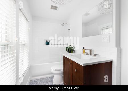 A white bathroom with a dark wood cabinet, mosaic tile floor, and a shower lined with white subway tiles. Stock Photo