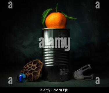 Still life with tangerine on tin can, glass ball and staple remover, studio shot, dark background Stock Photo