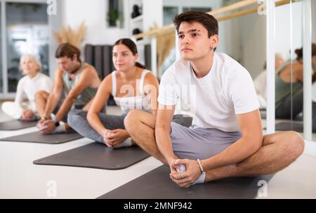 Positive athletic male performing set of exercises on a pilates mat during group class in fitness studio. Stock Photo