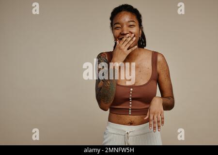 Candid portrait of ethnic young woman with tattoos laughing and covering face genuine emotion, copy space Stock Photo